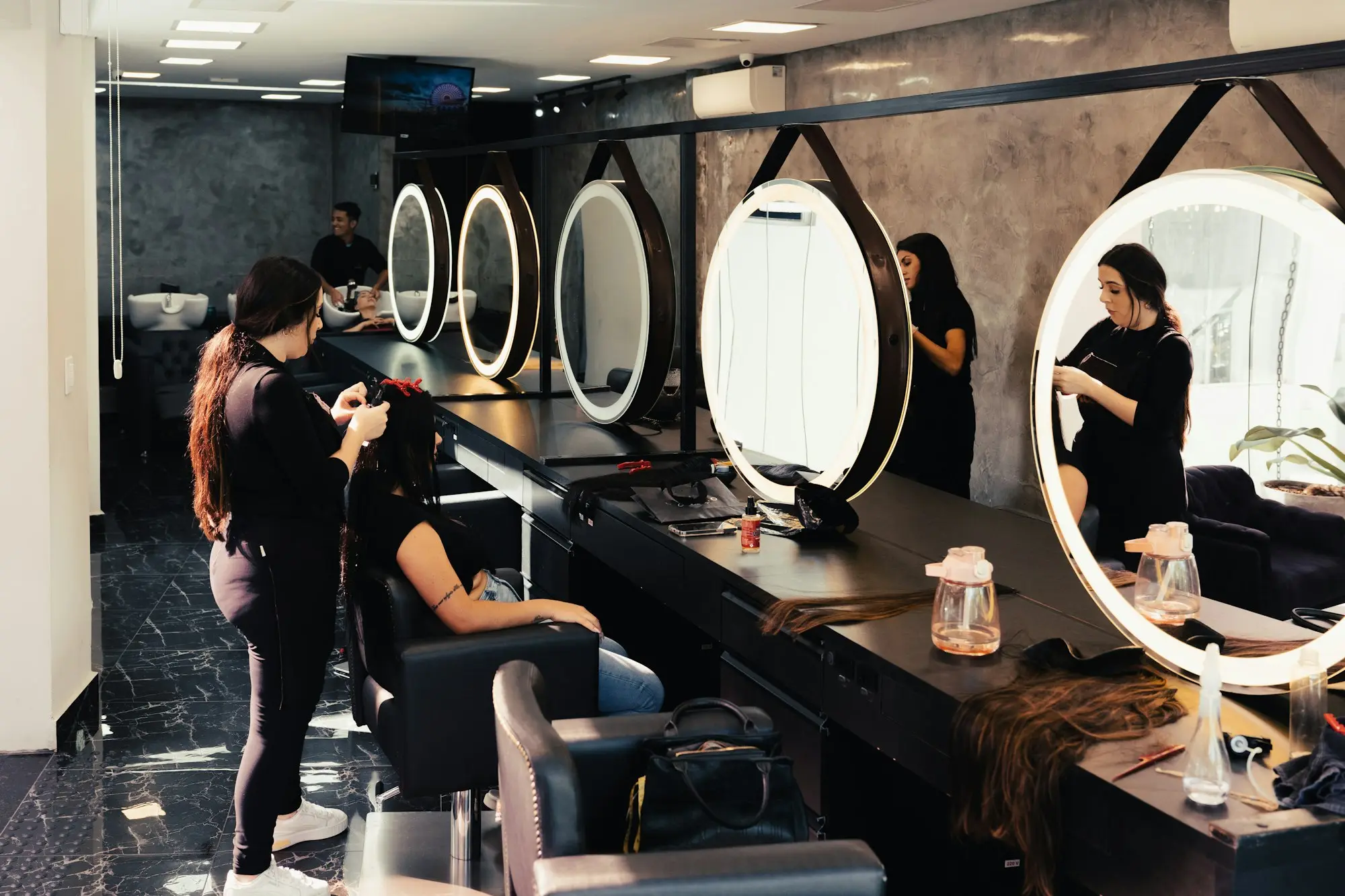Hairdresser styling a client's hair in a busy salon with round lit mirrors, the kind of card-paying business that gets in-app loan offers from its payment provider