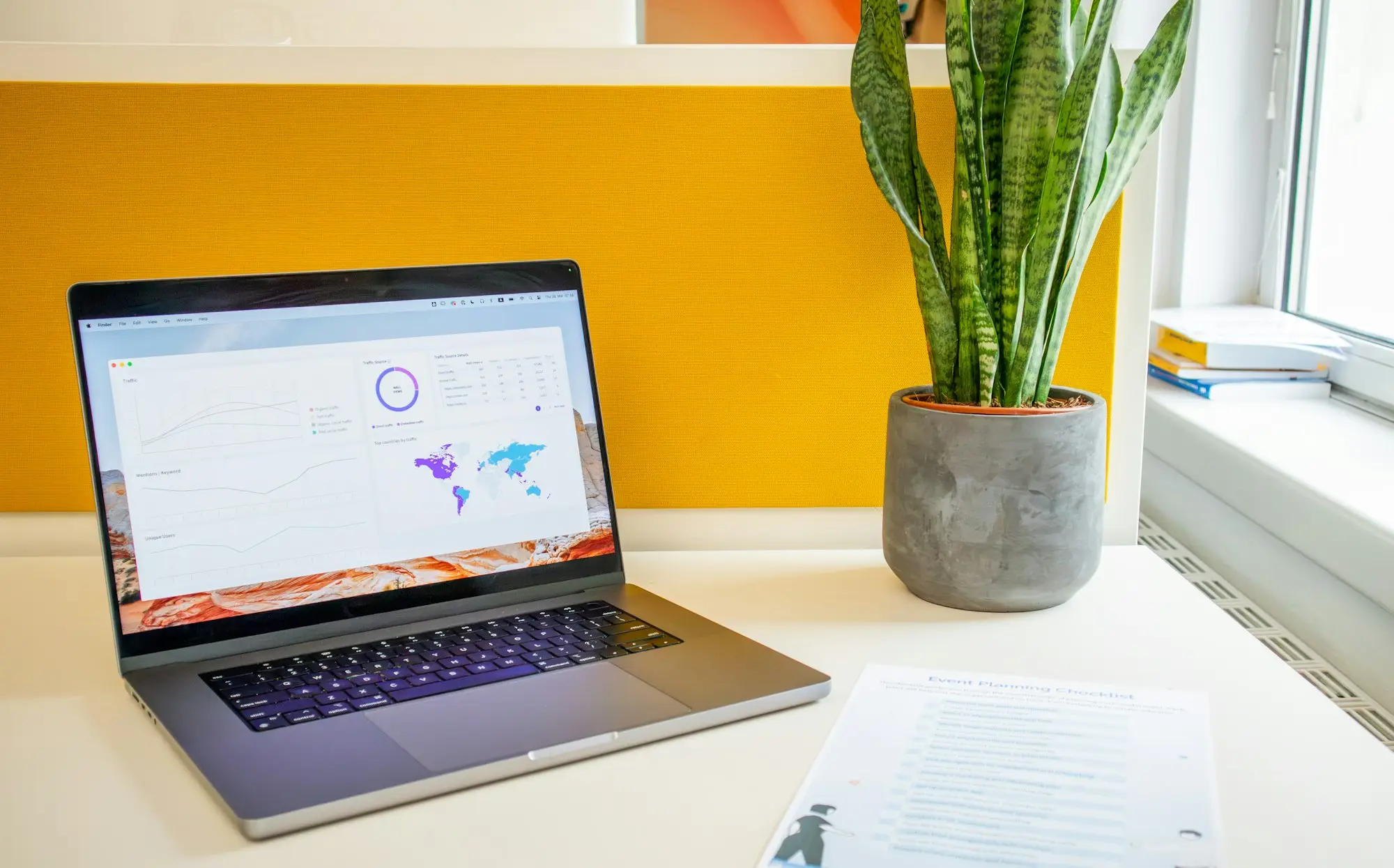 Laptop showing an accounting dashboard on a desk beside a printed migration checklist and a pot plant